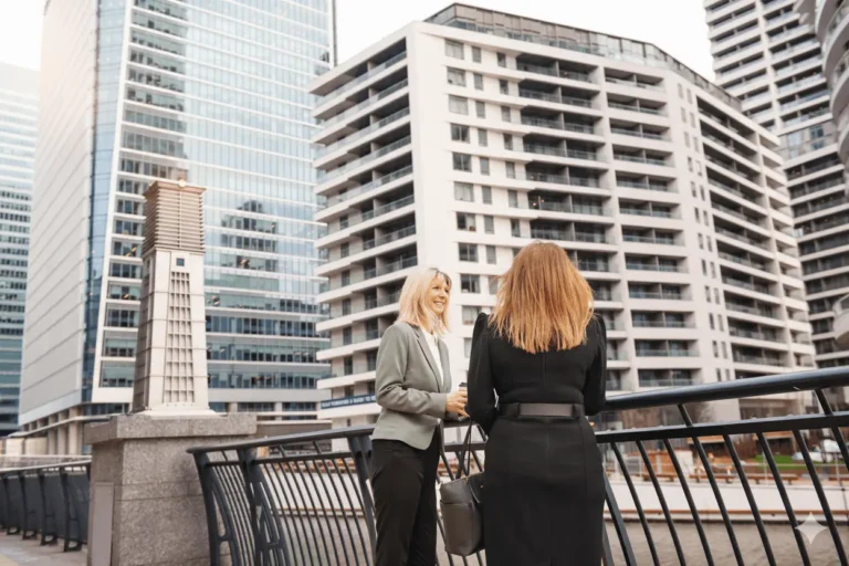 Two businesswomen discussing commercial property loans in front of modern office buildings
